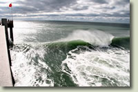 image: pier, red flag, big wave, clouds